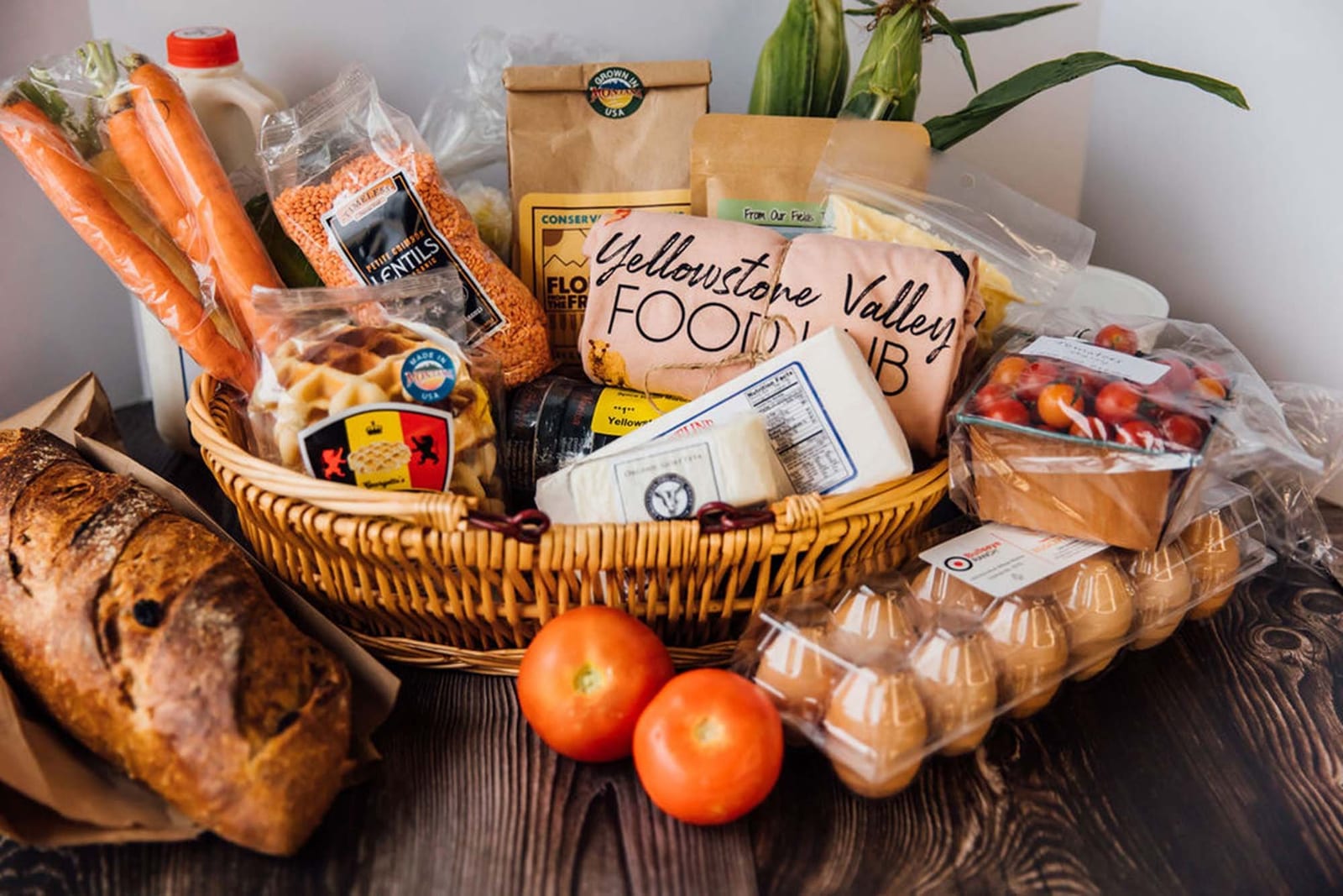 A basket of bread, eggs, carrots and packaged goods with a Yellowstone Valley Food Hub bag.