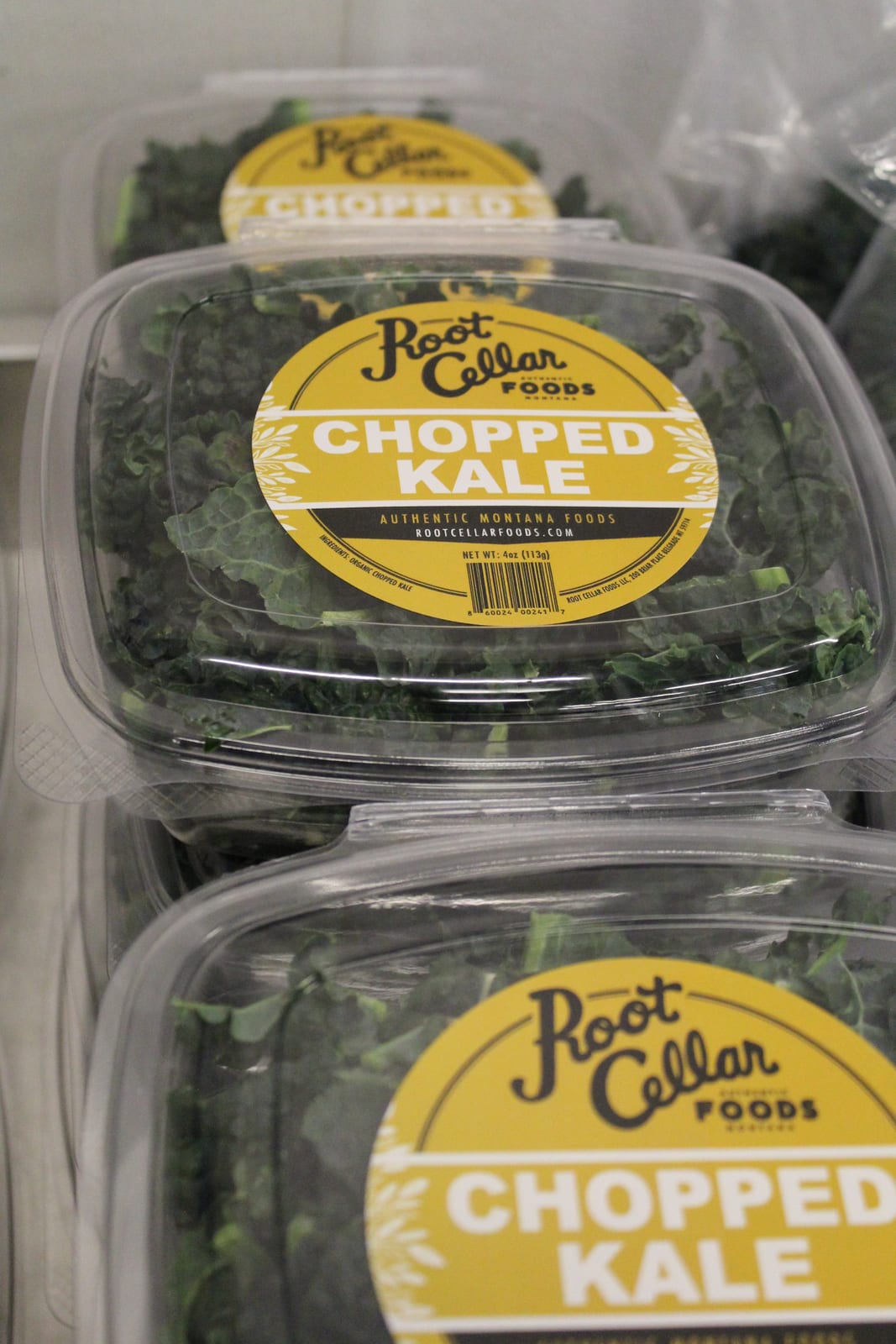 Stacked clamshells of chopped kale carrying the Root Cellar Foods label.