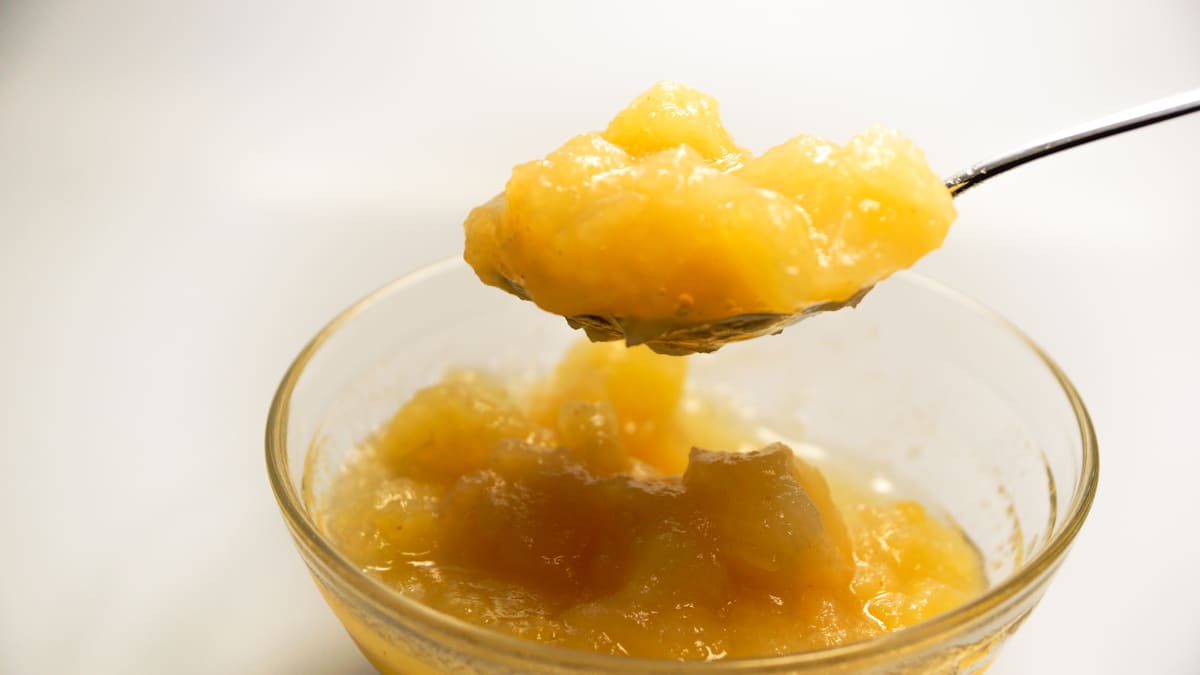 A spoonful of chunky applesauce lifted from a small glass bowl of applesauce.
