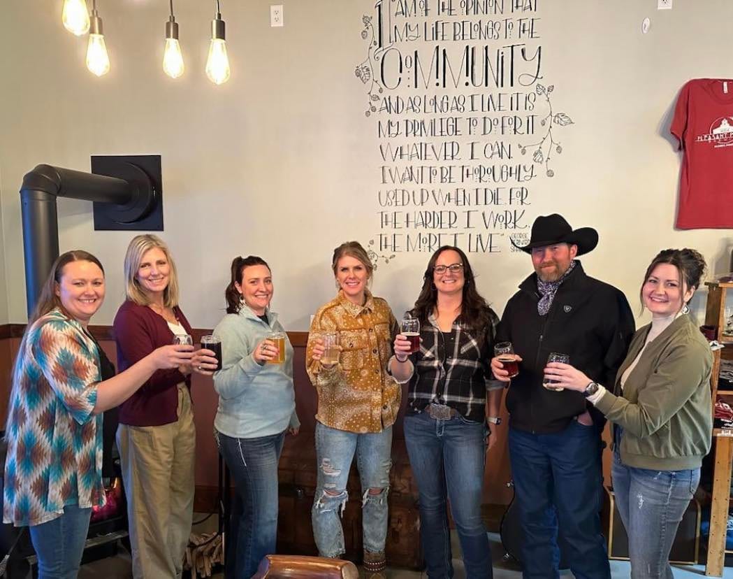 Seven Rolling Plains Co-op members raising glasses in front of a painted community mural.