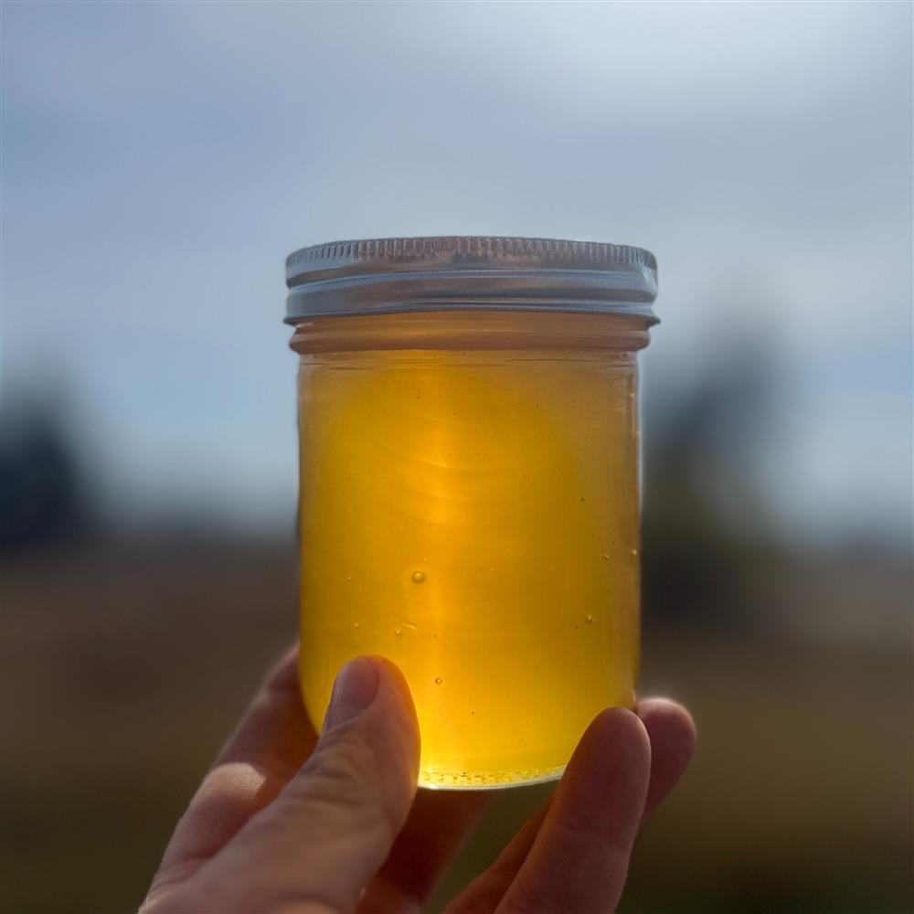 A hand holding a jar of golden honey against the light.