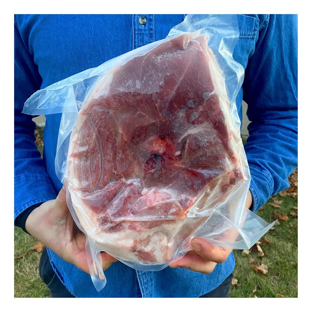 A person holding a packaged fresh ham roast.