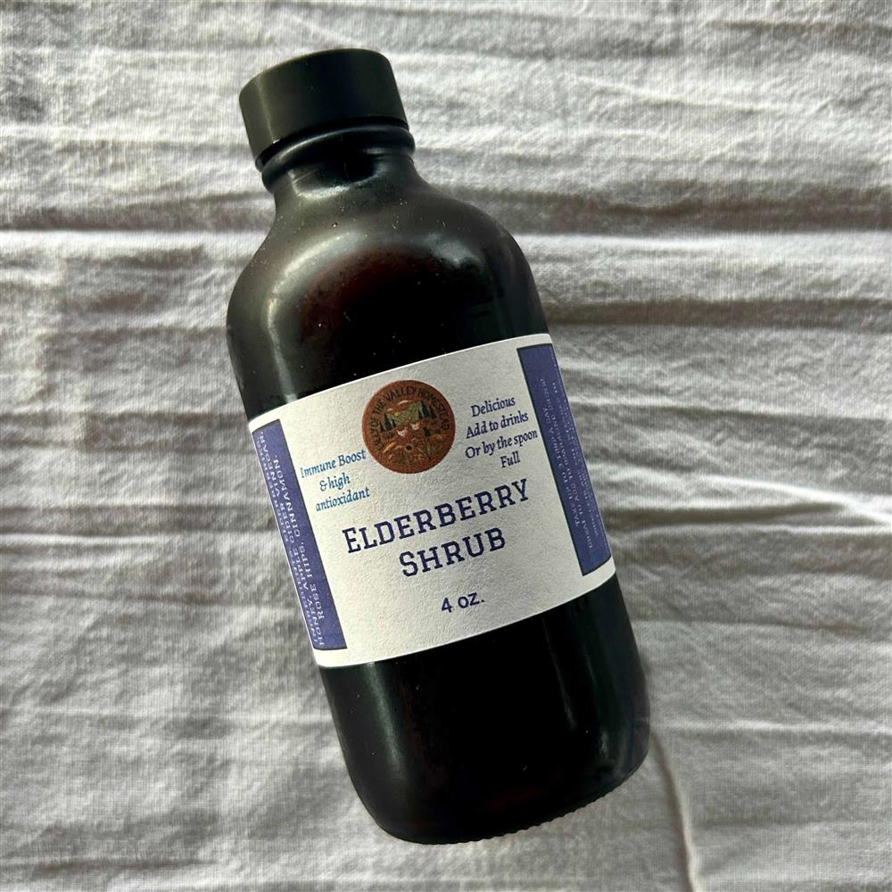 A dark bottle labeled Elderberry Shrub on fabric.