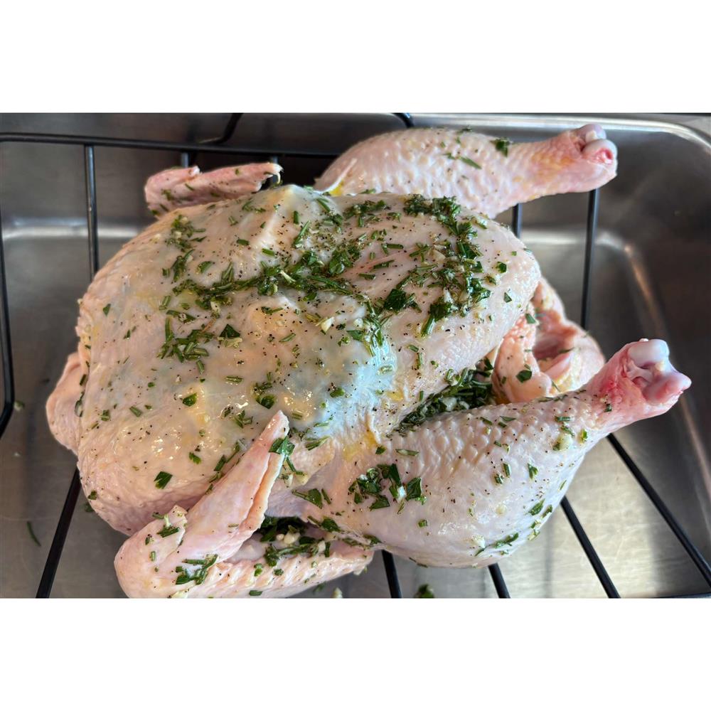 A whole chicken with herbs on a roasting rack.