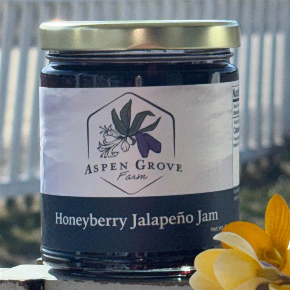 A jar labeled Honeyberry Jalapeño Jam beside yellow flowers.