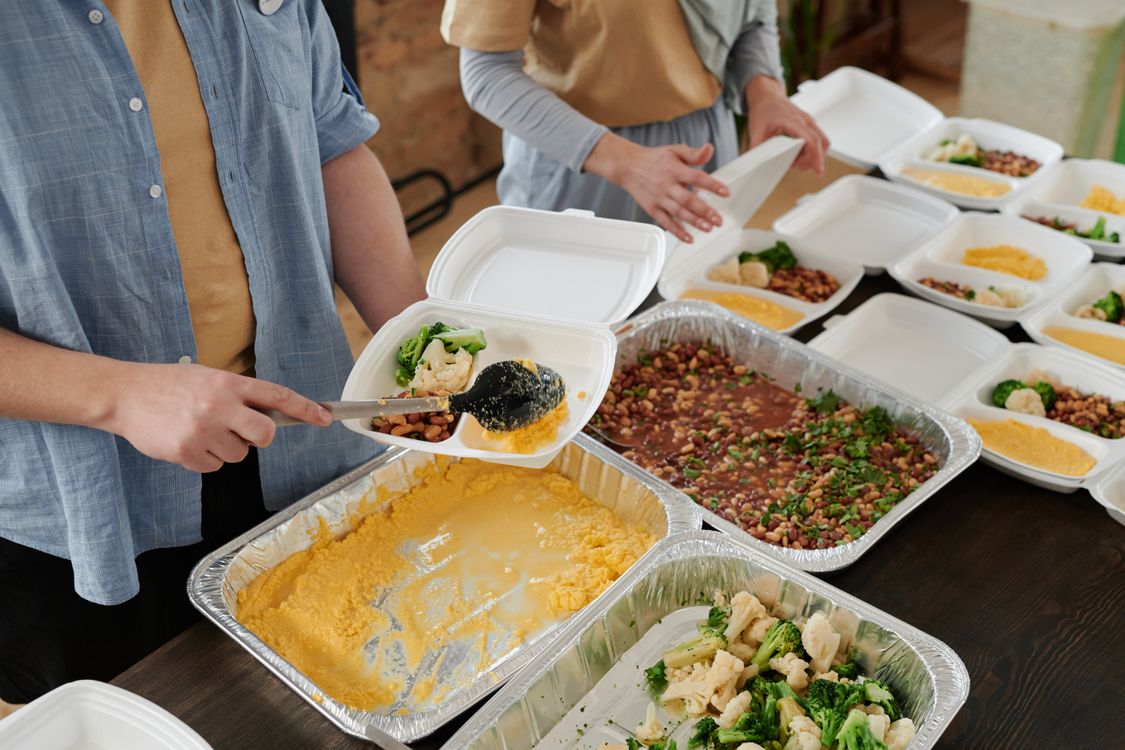 People portioning food into takeaway meal containers.